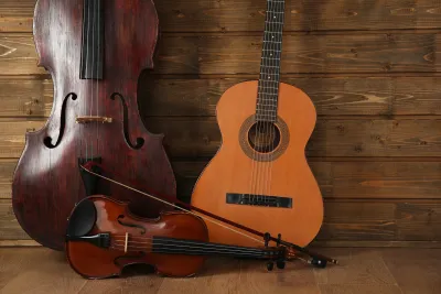 Cello, acoustic guitar and violin with bow leaning against a wooden plank wall