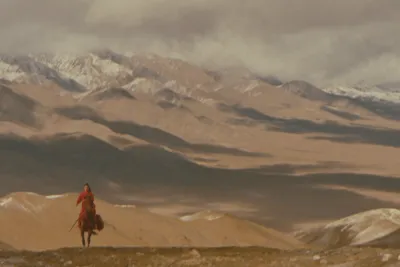 Film still from Hero: a lone rider in red crossing a vast mountain landscape