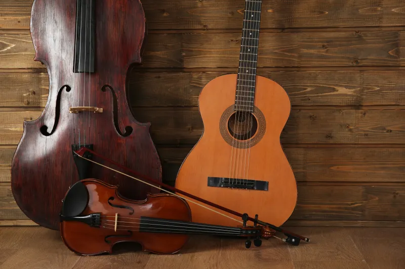Cello, acoustic guitar and violin with bow leaning against a wooden plank wall