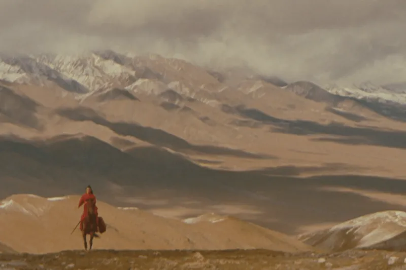 Film still from Hero: a lone rider in red crossing a vast mountain landscape
