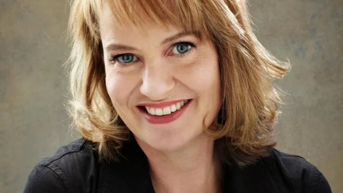 Portrait of composer Anne Dudley smiling, with shoulder-length blond hair
