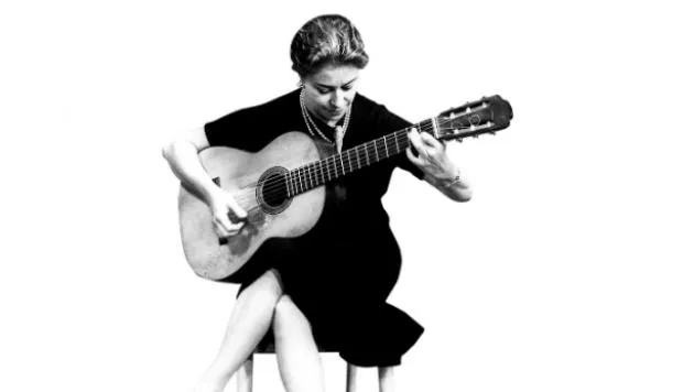 Black-and-white photo of Chabuca Granda seated on a stool playing a classical guitar