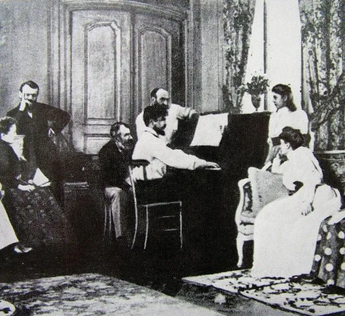 Black-and-white photo of Debussy at the piano in Ernest Chausson's salon with listeners around him