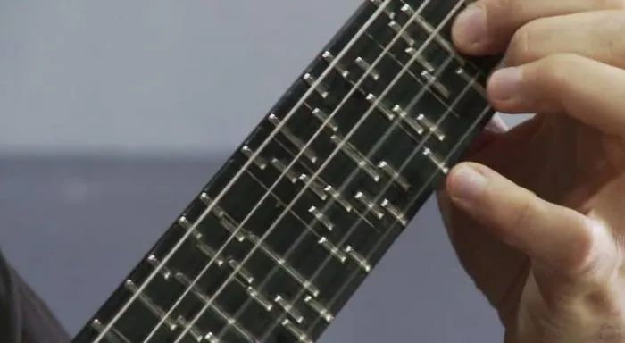 Close-up of a hand on a microtonal guitar fretboard fitted with many short movable frets