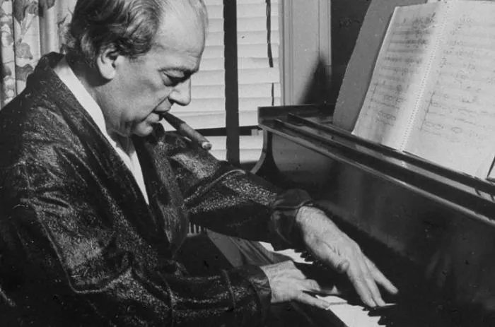 Black-and-white photo of Heitor Villa-Lobos playing piano in a dressing gown, cigar in mouth