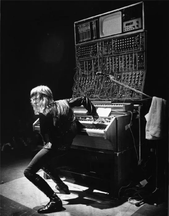 Black-and-white photo of Keith Emerson on stage bending at an organ beneath a giant Moog synthesizer