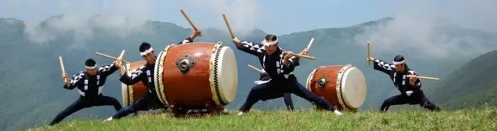 Kodo drummers striking large taiko drums on a misty green hilltop