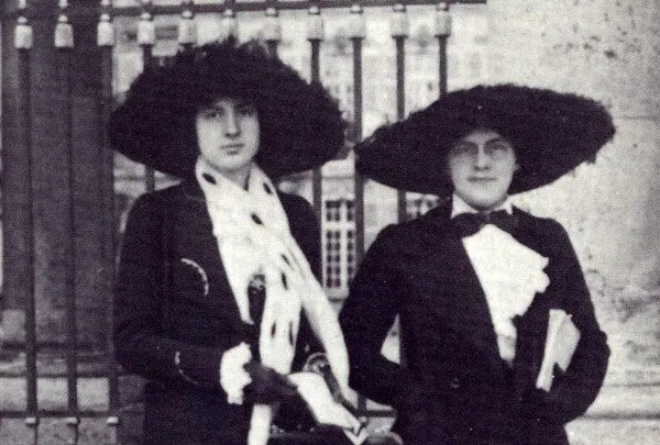 Black-and-white photo of sisters Lili and Nadia Boulanger in large dark hats by an iron gate