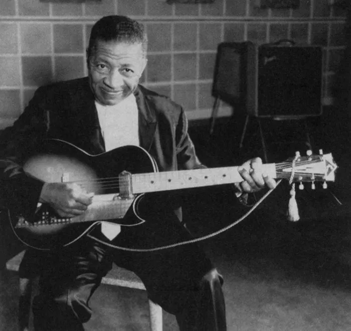 Black-and-white photo of an older Lonnie Johnson smiling with an archtop electric guitar