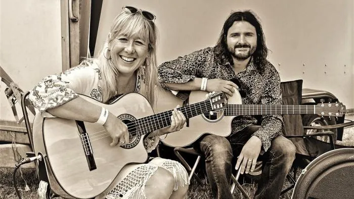 Sepia photo of the duo Oka Vanga, Angela and Will, seated with acoustic guitars