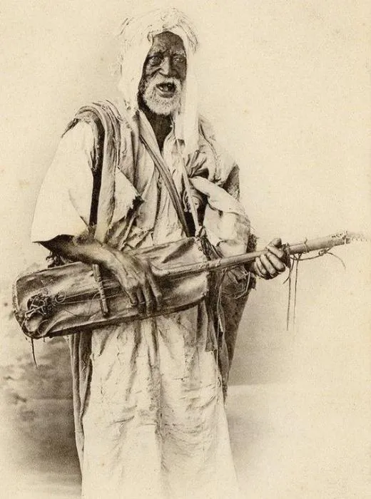 Sepia photo by Jean Geiser of an elderly Gnawa musician from Algiers playing a guembri