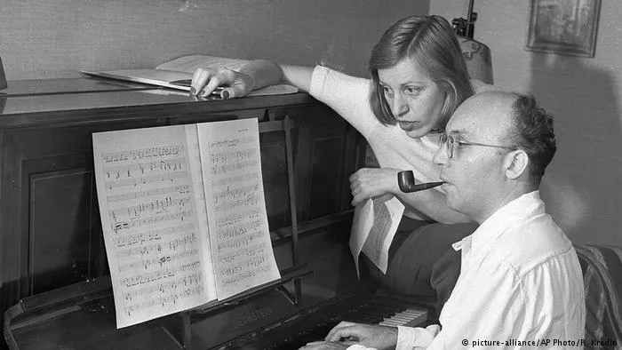 Black-and-white photo of Kurt Weill at the piano with a pipe, a woman beside him